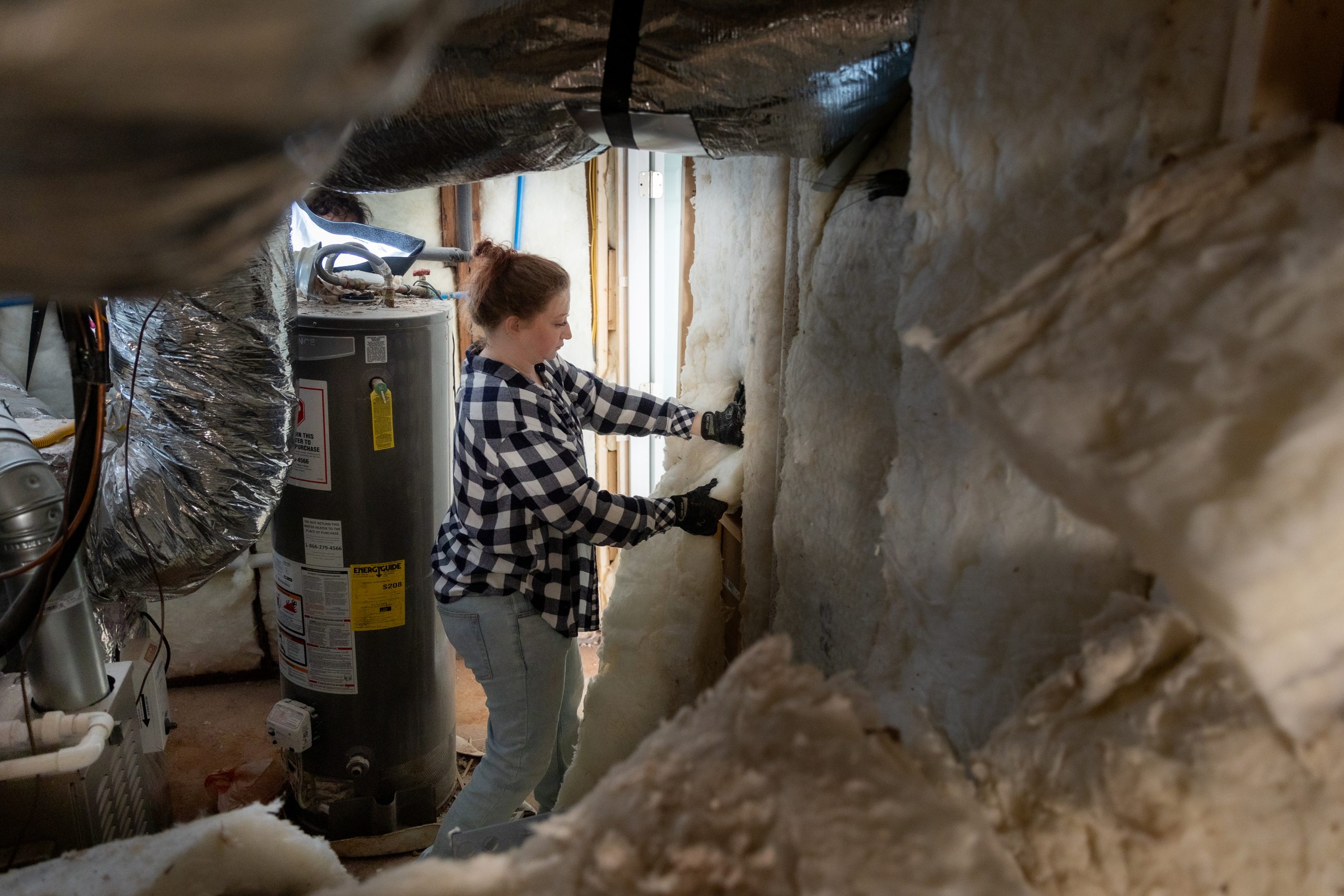 Caucasian female wearing PPE removing old insulation from a wall