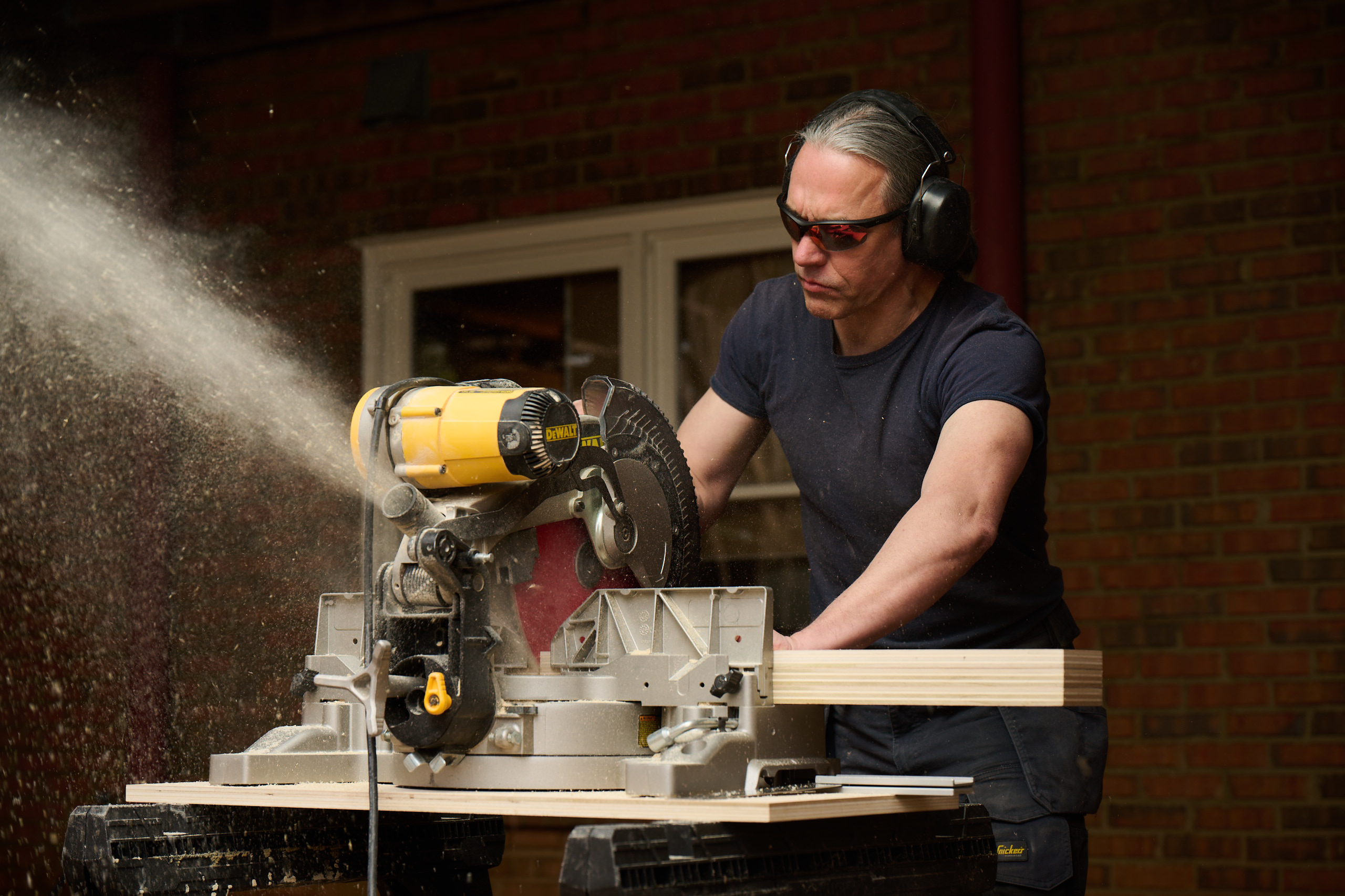 Caucasian male using a chop saw to cut a piece of lumber