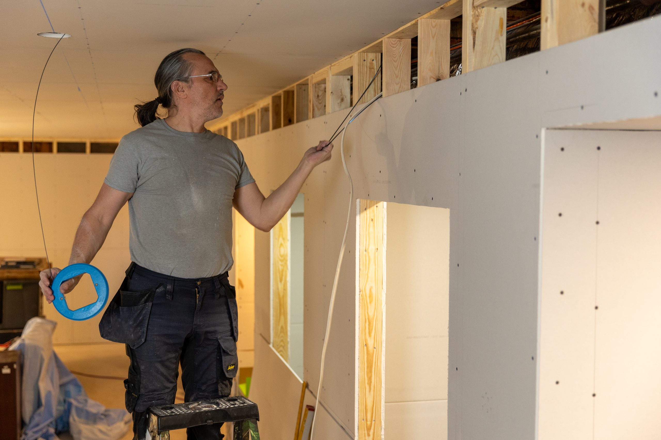 Caucasian male standing on a ladder, running electrical wiring