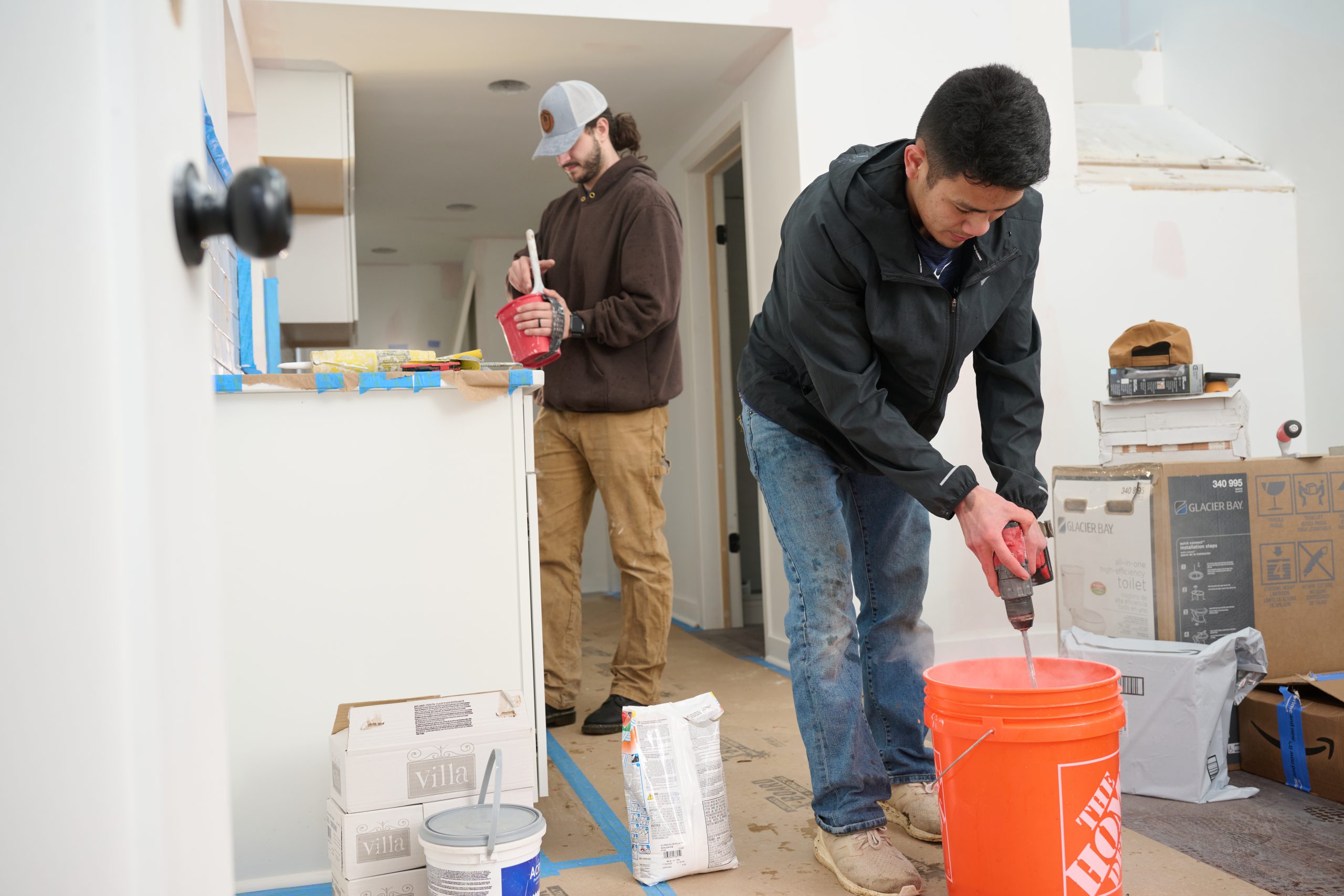 Asian male mixing paint in a bucket with another male working in the background
Why the Trades