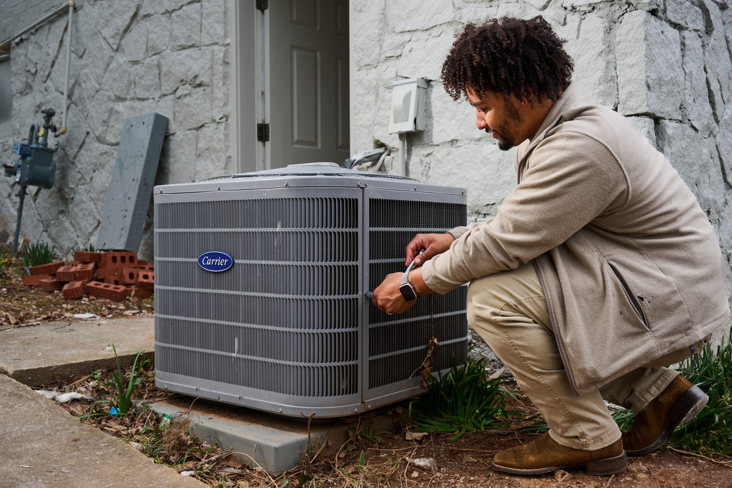 African American male kneeling down to work on an exterior HVAC fan unit