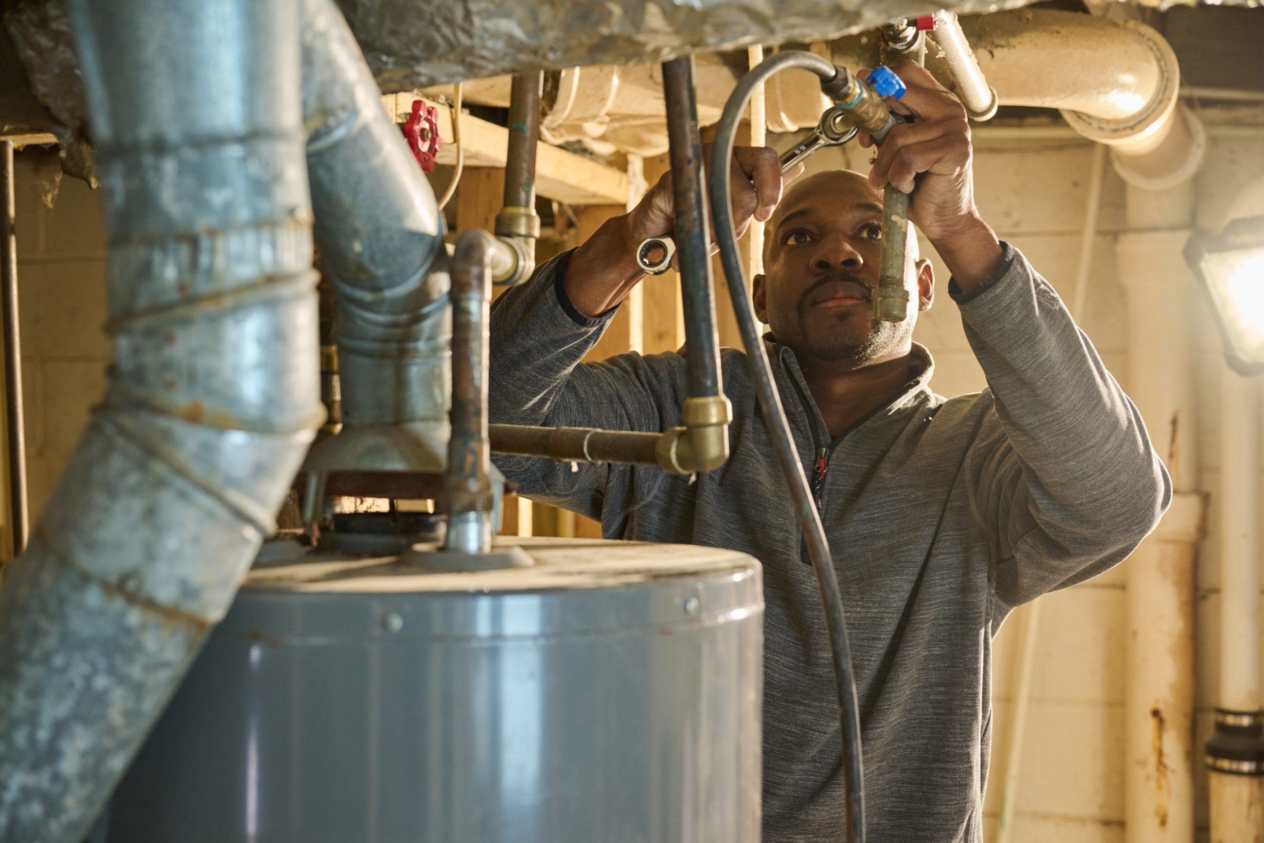 African American male using a wrench to fix a hot water heater