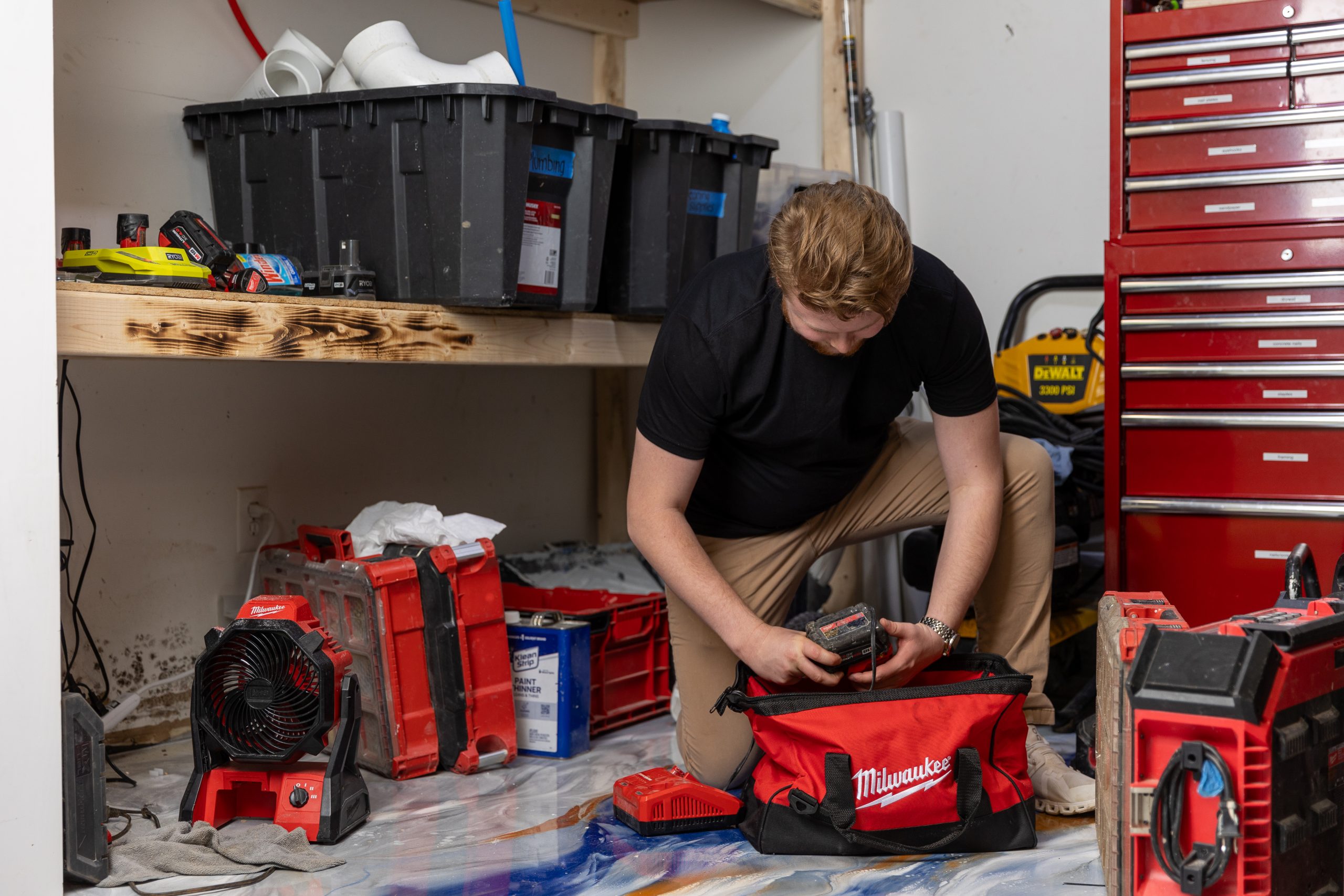 Caucasian male kneeling down packing a tool kit in a workshop